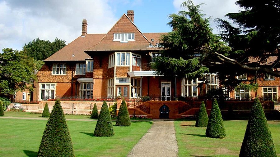 A red brick house with trees and a green lawn in the foreground
