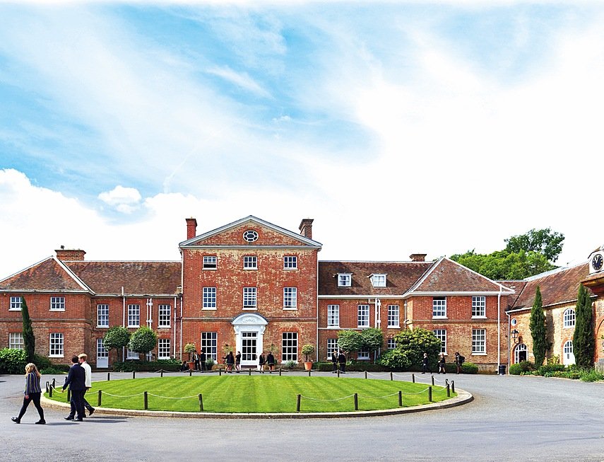Beautiful red-brick school house with round lawn in front around which pupils walk