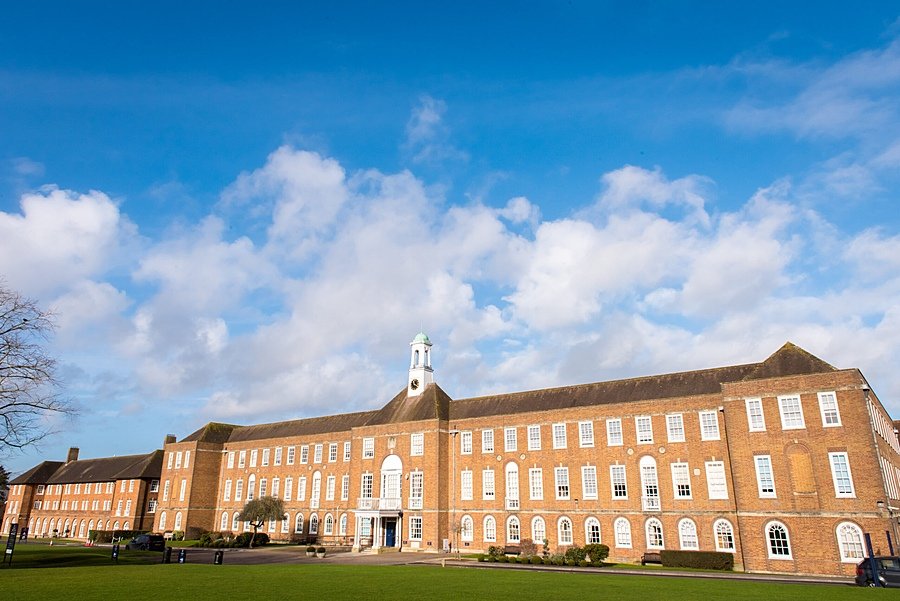 An imposing red brick school building with tower under a blue sky with clouds