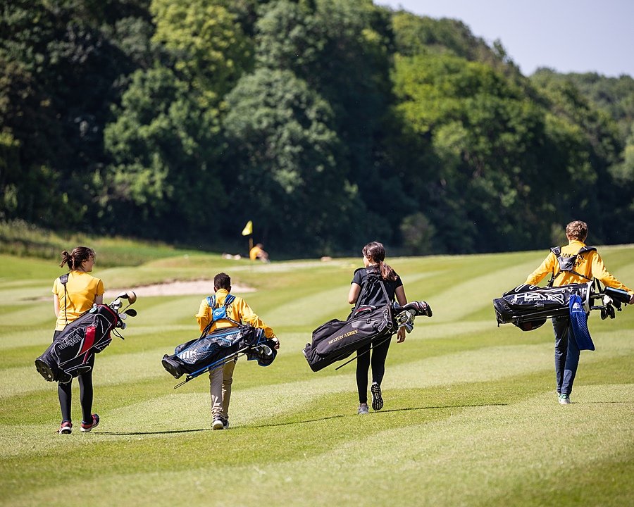 four golf players on the golf course from behind carrying their heavy golf bags