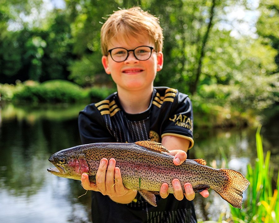 A boy with glasses holding proudly a trout into the camera during Sedbergh International Summer School