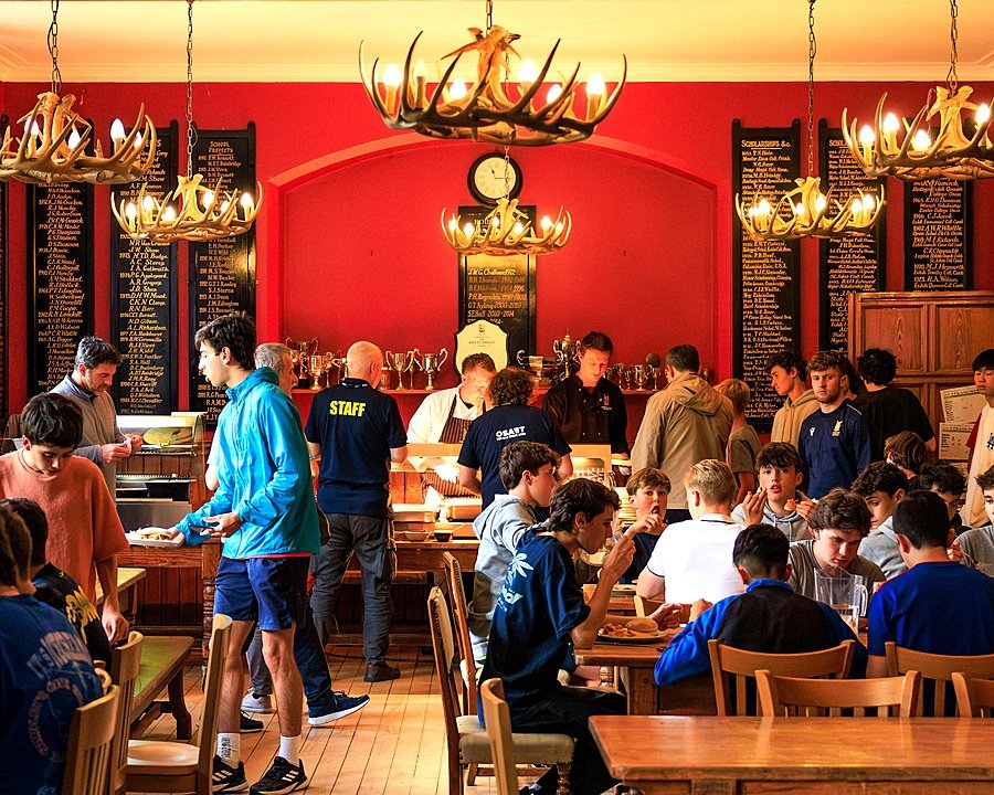 Students eating together in the cosy dining hall with red walls during Sedbergh International Summer School