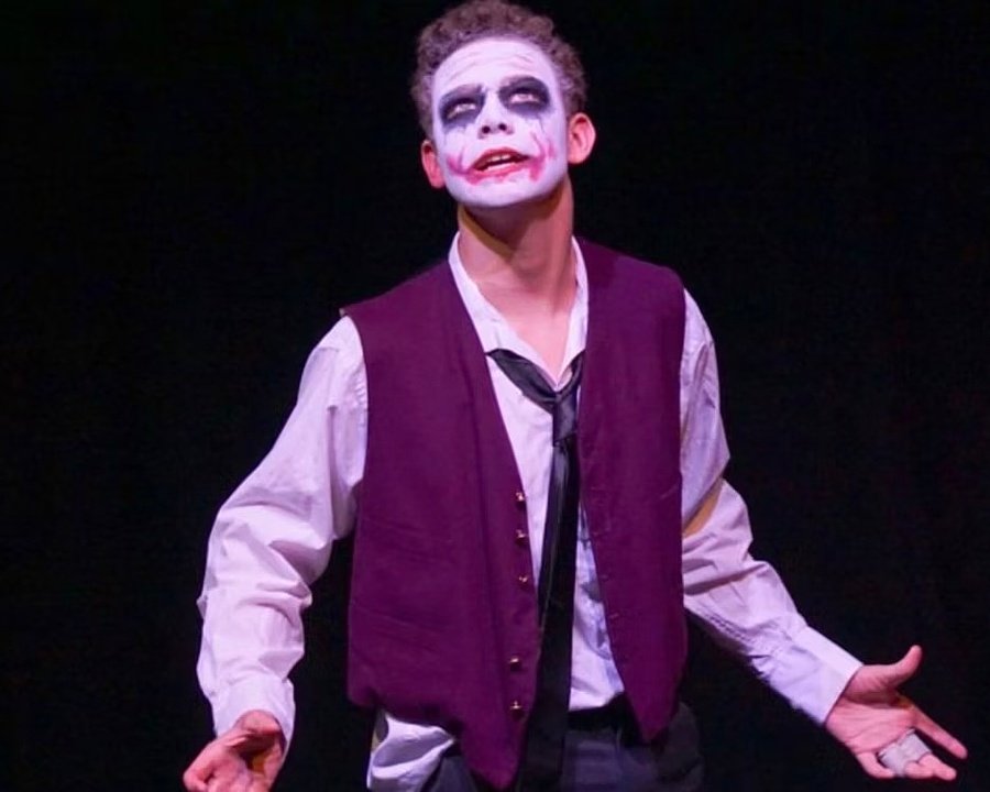 A young actor wearing face paint resembling the Joker character performing on stage.