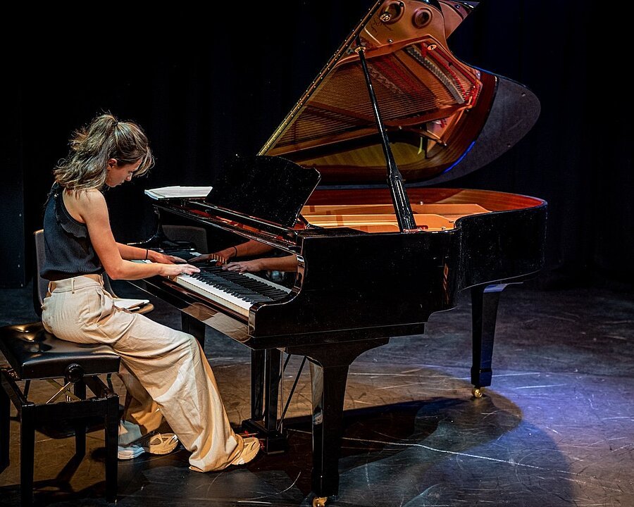 A student playing a grand piano on stage under soft lighting.