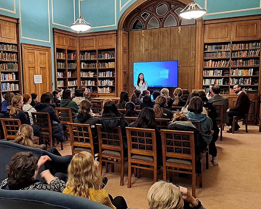 A group of girls sitting in a library, listening to a teacher giving a talk