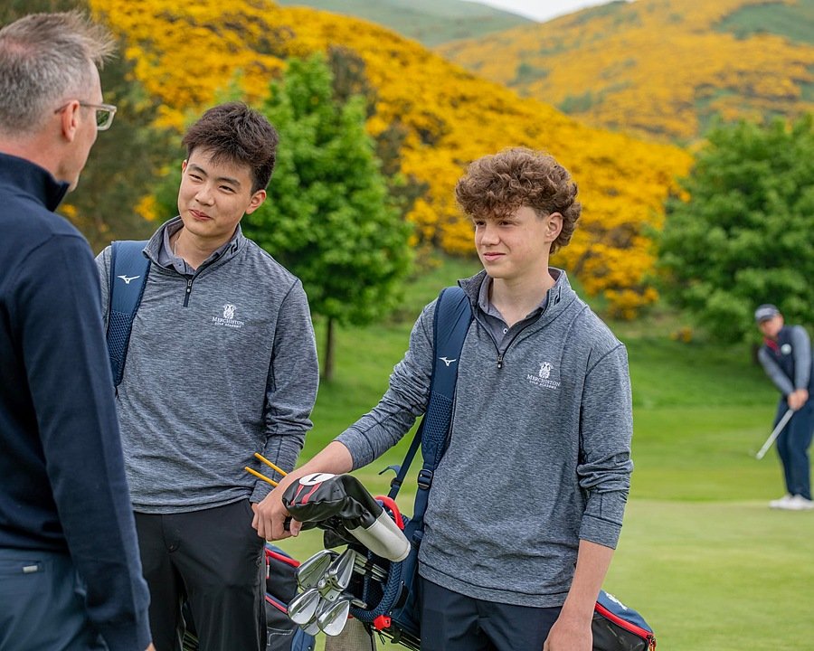 Two boys and a man having a chat. One boy carries a bag with golf sticks in it