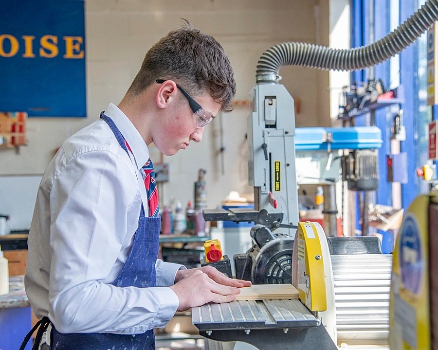 A boy with safety-goggles on working on a wood-saw