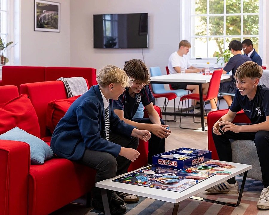 Boys in school uniform sitting on red sofas over a game of Monopoly