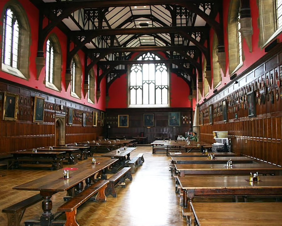 Large hall with long tables, wood beam ceiling, red walls, and a large window