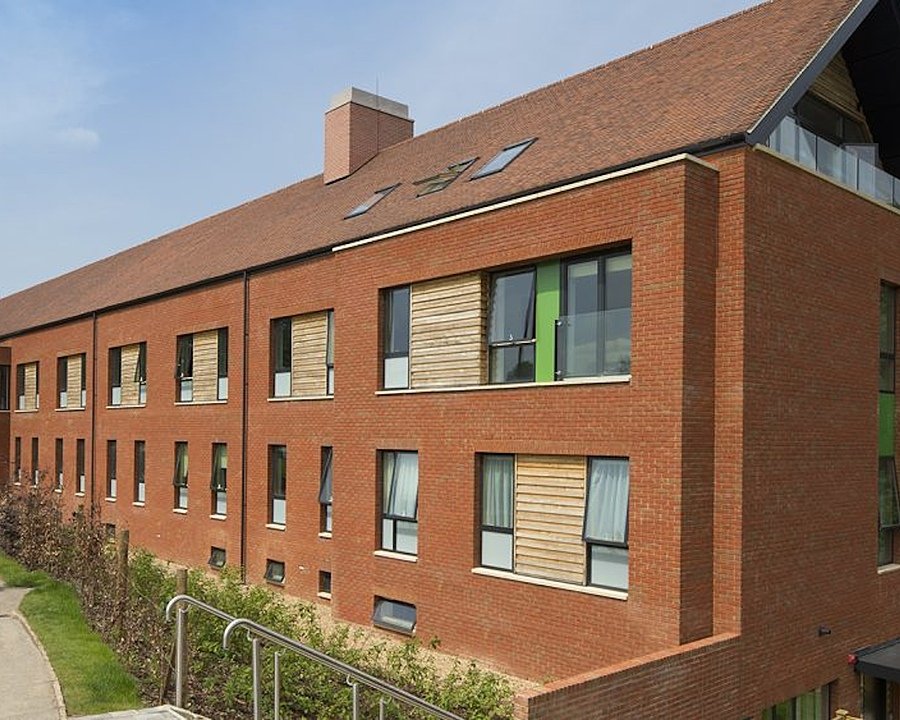 A modern red brick building with wood-paneled shutters and two boys walking next to it
