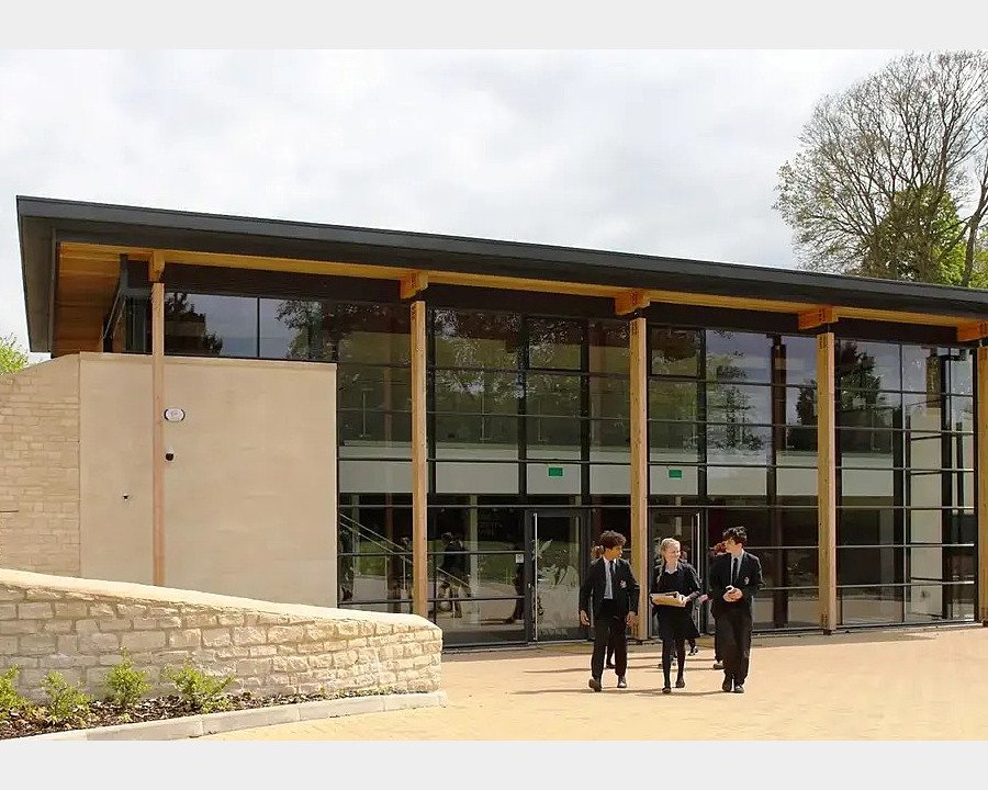 Modern building with flat roof and high glass windows with three pupils walking away from it.