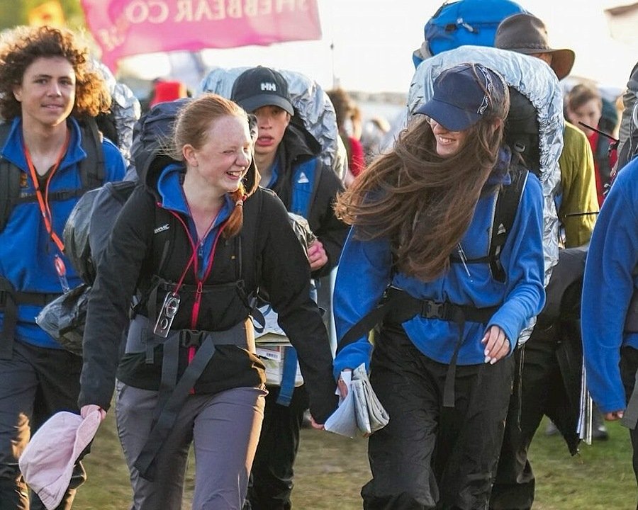 Youths with rucksacks and rain gear leaving a camping ground, laughing
