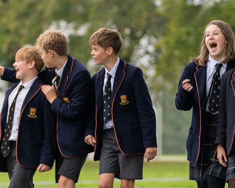 Six children in school uniform walking across school campus, whilst laughing