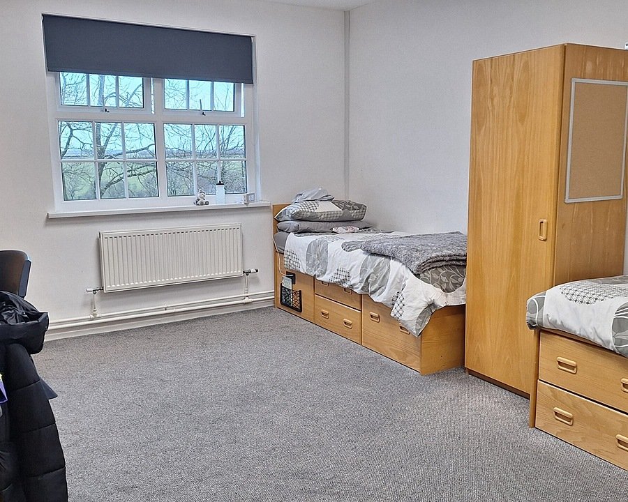 A spacious boarding room with two beds, a desk, a cupboard and a window