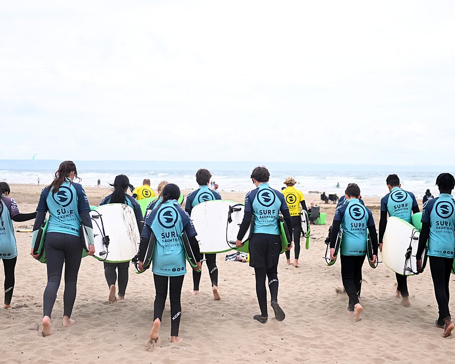 Boarding school students in wetsuits walking along the beach during an outdoor education programme