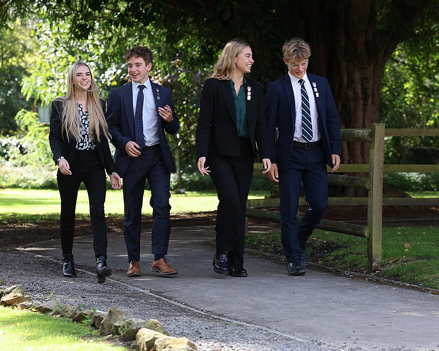 two male and two female students in their school uniforms walking through a park