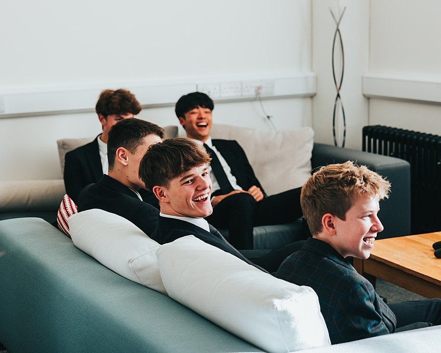 Boys in school uniform sitting in common room laughing