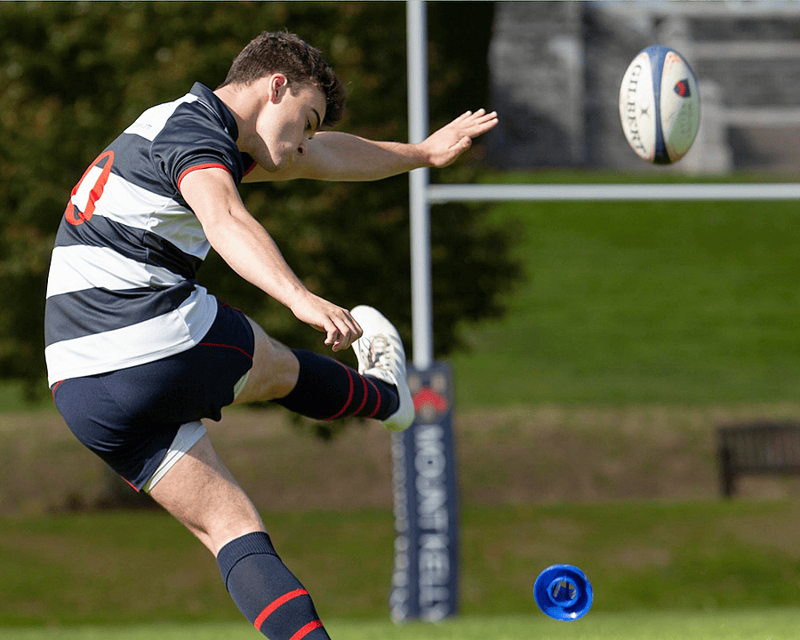 Pupil kicking a rugby ball over a distant rugby goal