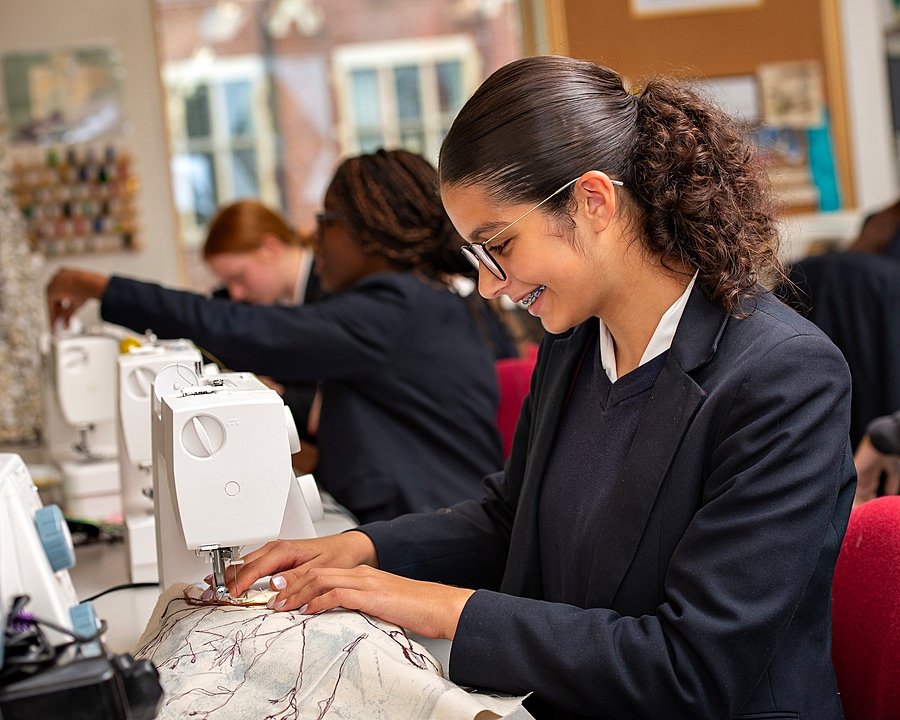 Student concentrating and smiling while using a sewing machine in a classroom.