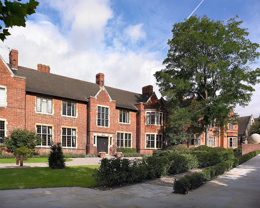 Traditional red-brick school building with neatly trimmed hedges and pathway in front.