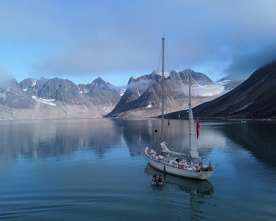 a white two-master in a fjord with snowy mountains in the background