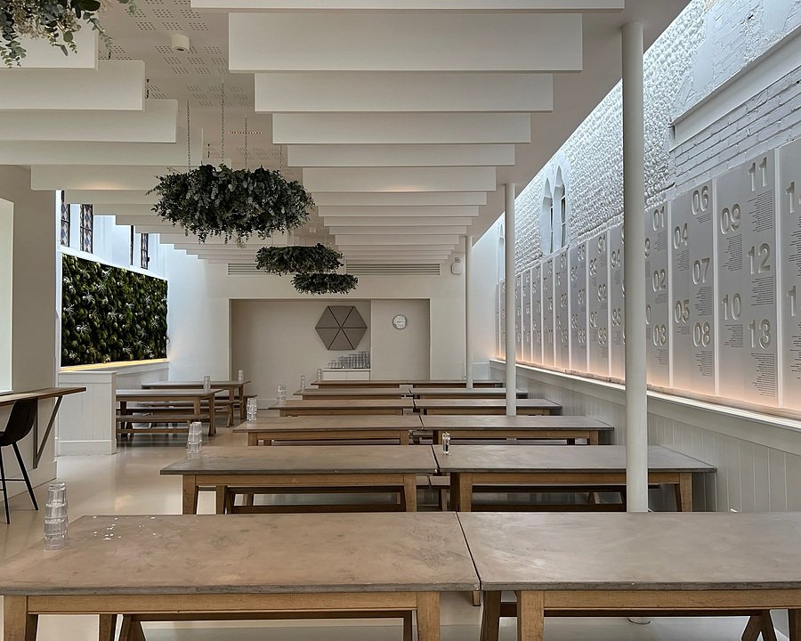 Bright modern dining hall with wooden tables, green wall, and hanging plants.