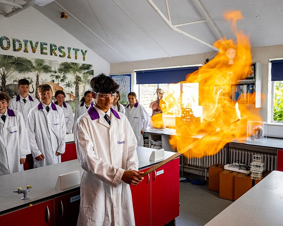 A chemistry student in front and his peers behind him in the science lab is holding a burning stick in front of him