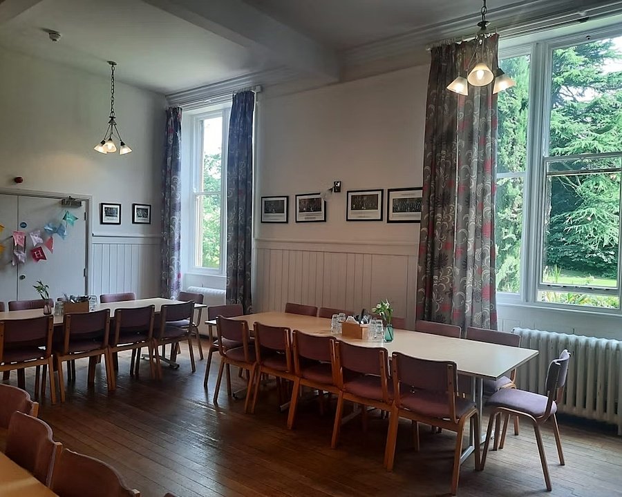 A dinding hall with big windows and long wooden tables and chairs