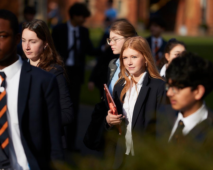 Students in formal school uniforms walking together outdoors on a sunny day.