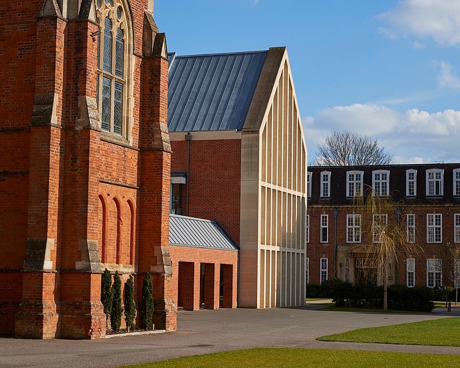 Historic red-brick school buildings with tall windows and a modern extension featuring light stone columns.