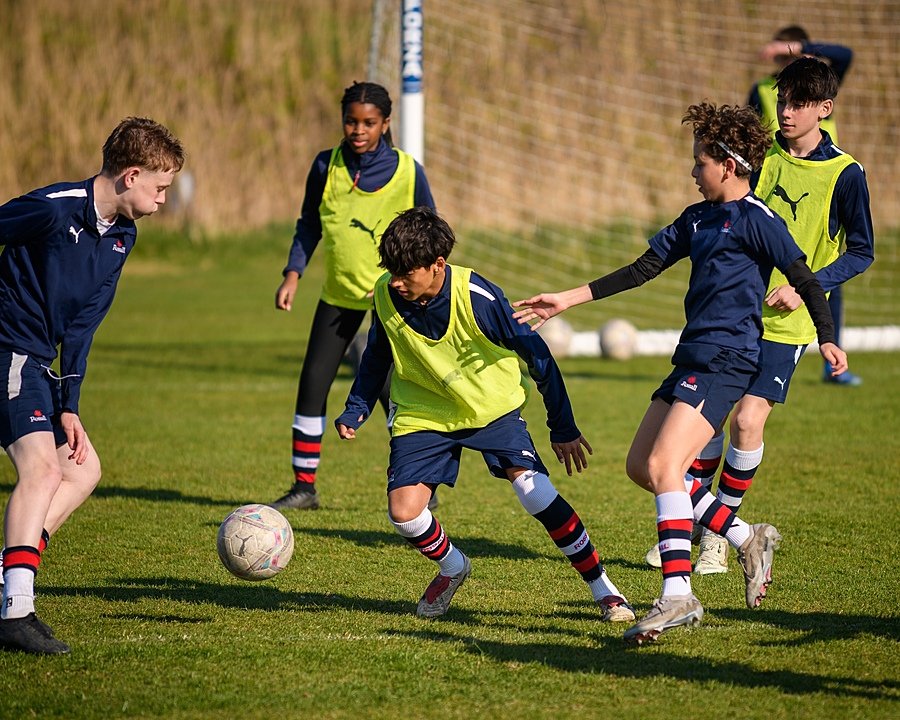six boys outside in a game of football during their training