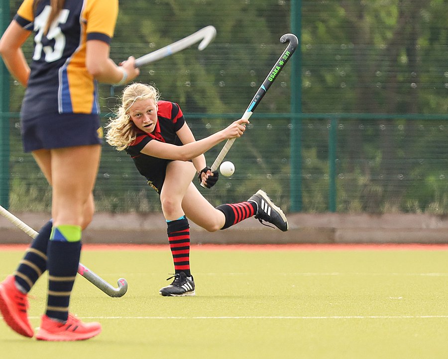 Two girls in hockey jerseys with hockey sticks as part of a hockey match