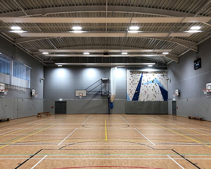 Sports hall, well lit with basketball hoops and a climbing wall in the background