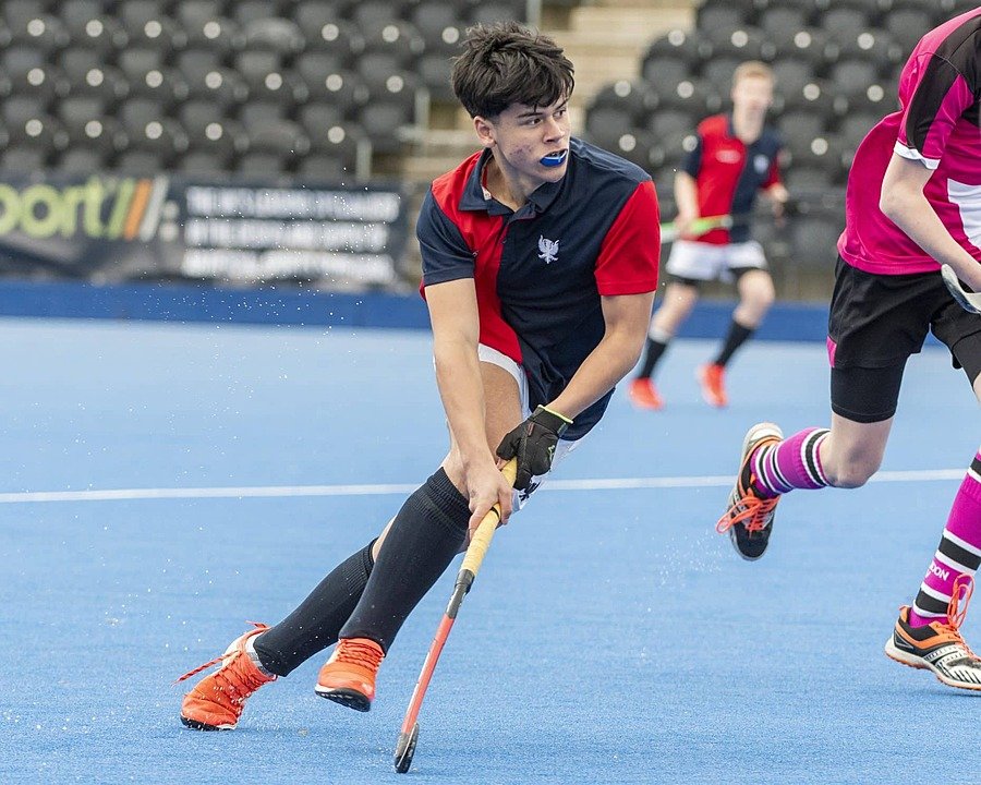 Boy in hockey jersey on a pitch mid-play, wearing mouth guard