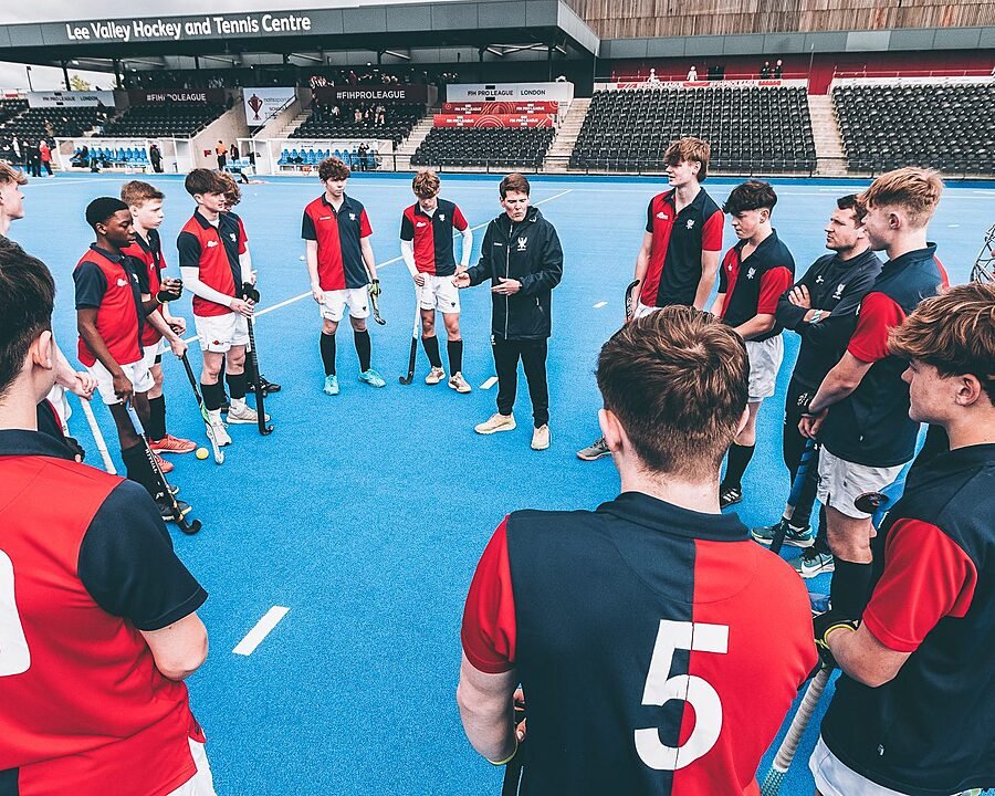 Boys in hockey jerseys standing in circle around a coach, giving instructions