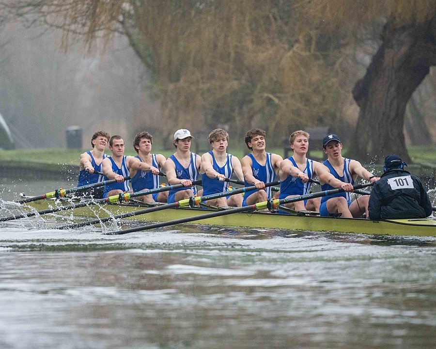 Rowing boat on a river with eight boys mid-row on a grey day