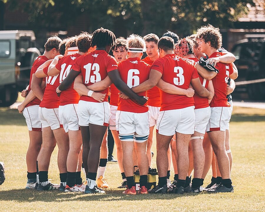 Boys in red rugby jerseys in a circle with arms around each other, having a team conversation