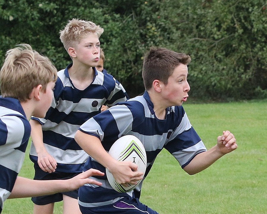 Three boys in striped jerseys and a rugby ball running on a field