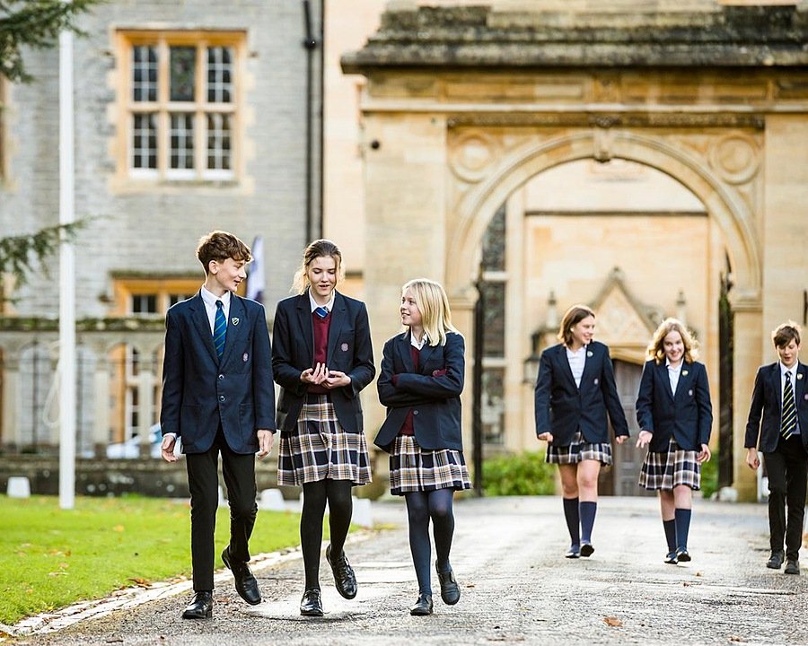 Six pupils in school uniform chatting and walking away from a school building