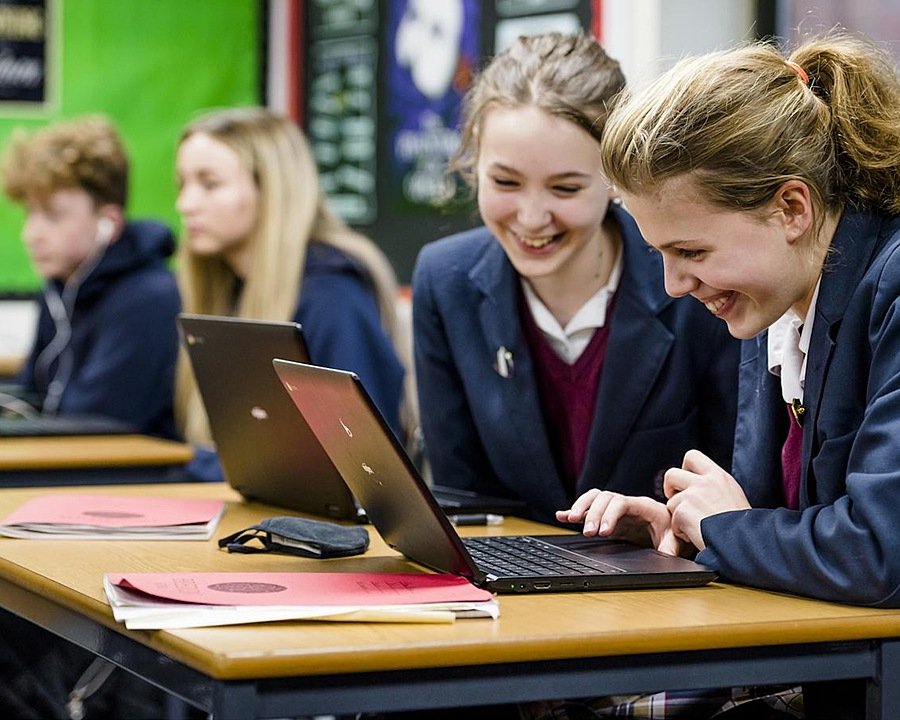 Two girls in school uniform looking at a laptop schreen, smiling