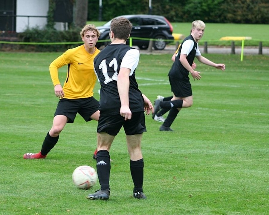 Students playing football on a green field, wearing black and yellow sports kits.