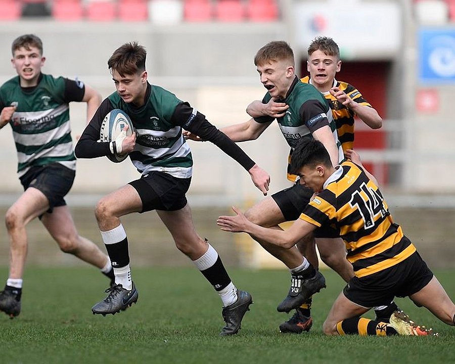 A group of pupils playing rugby, with one player running forward holding the ball while opponents attempt to tackle.
