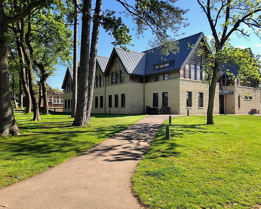 Modern school building with stone walls and a metal roof surrounded by trees and green lawns.