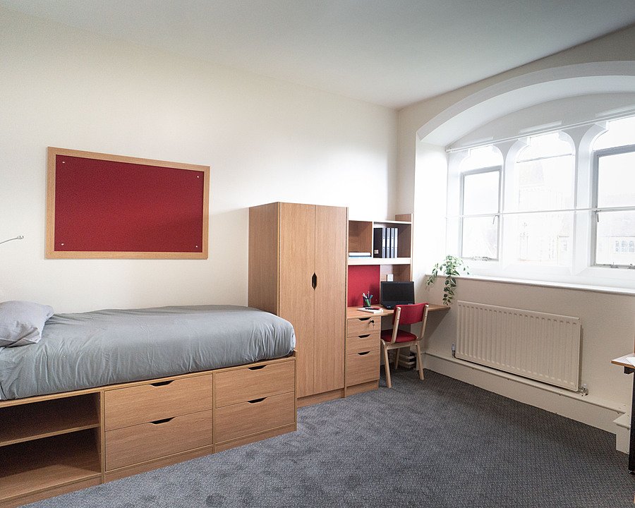 A spacious, well-lit boarding room with modern low bed, cupboard and desk