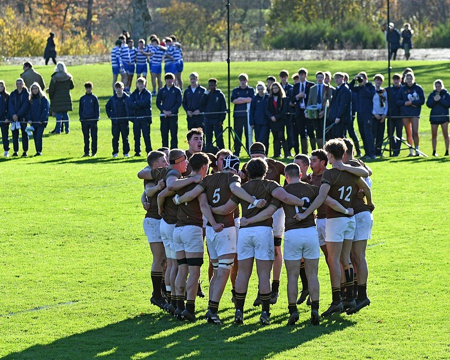 A rugby team in brown and white uniforms gathers in a huddle on the field before a match.