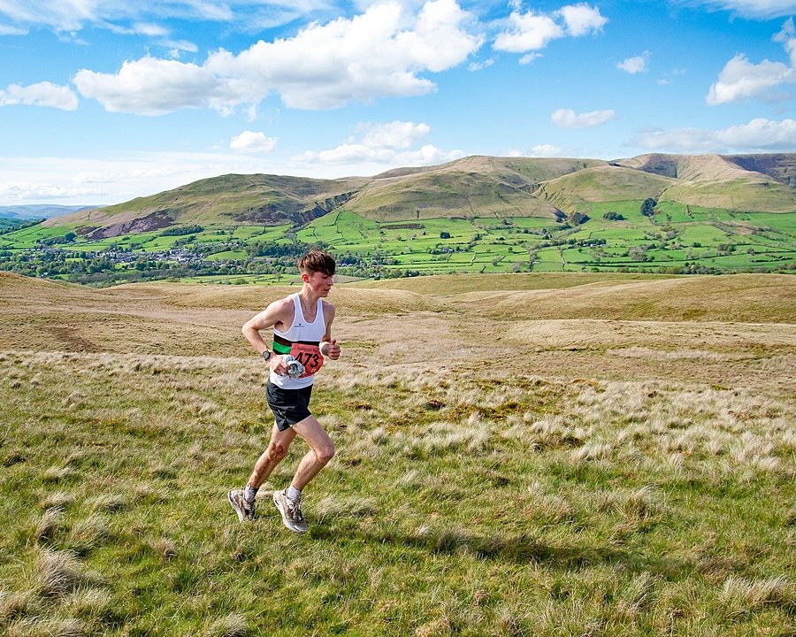 A runner in a race crosses grassy hills with scenic green valleys and mountains in the background.