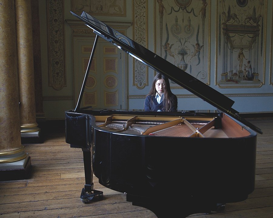 Student playing a grand piano in an ornate room with decorative walls and tall columns.