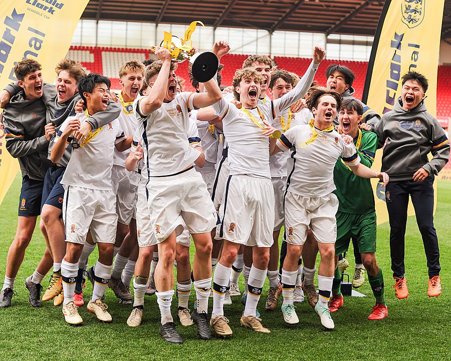 A jubilant football team celebrating victory on the pitch, holding a trophy.