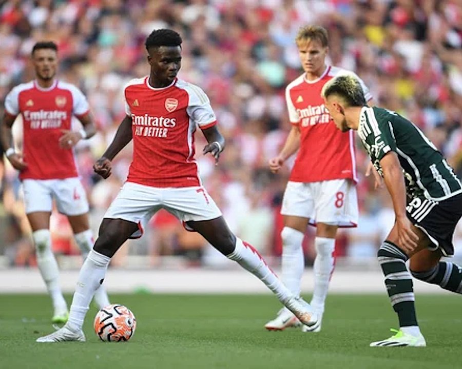 A football player in a red and white uniform controls the ball during a match, with teammates and opponents visible in the background.