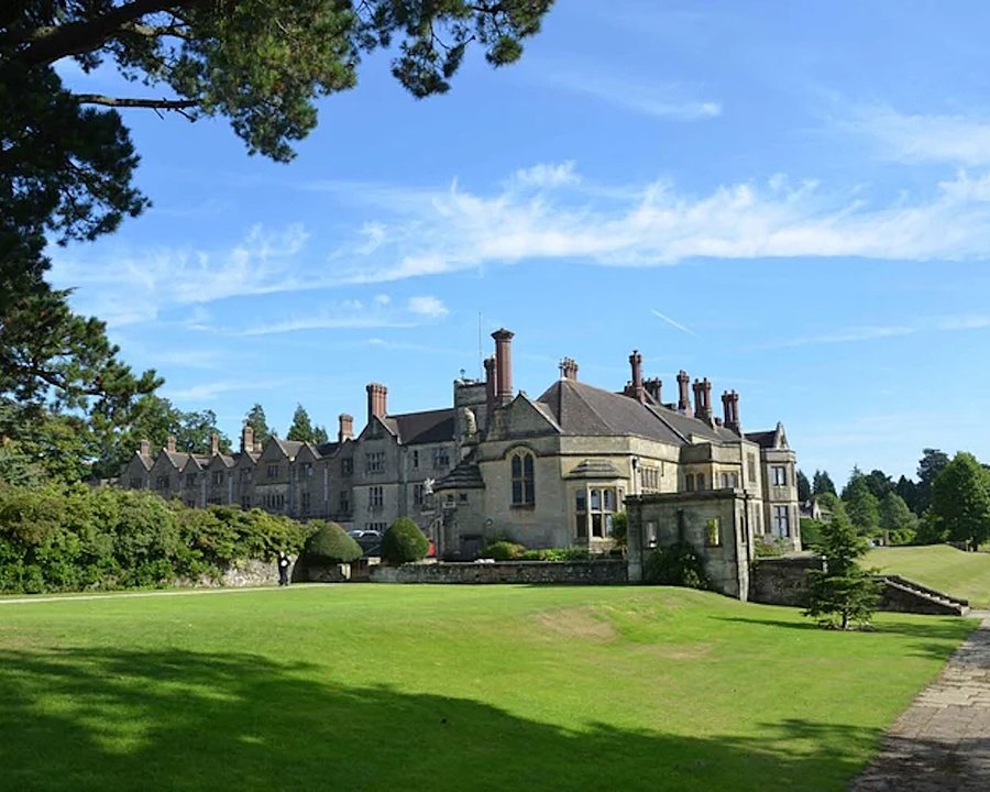 A historic stone school building with gardens and manicured lawns under a bright blue sky.